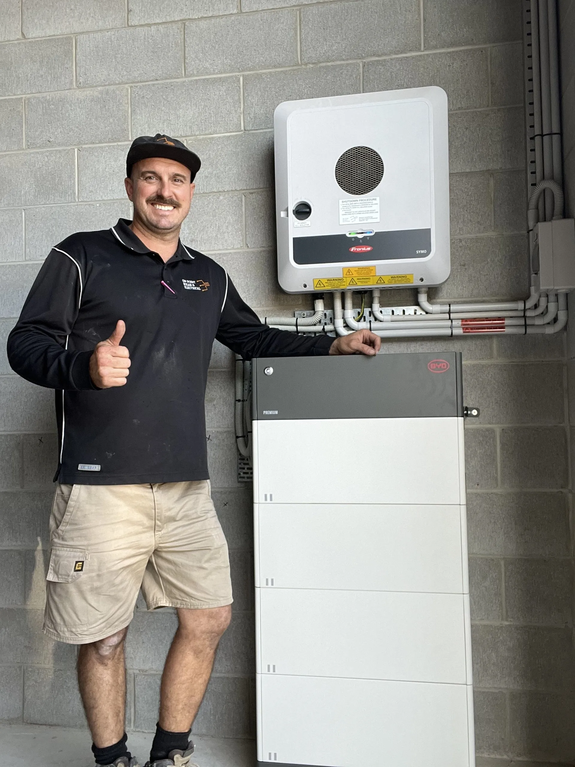 On Point Solar & Electrical owner Jason beside a Fronius inverter and BYD solar battery installed in Townsville