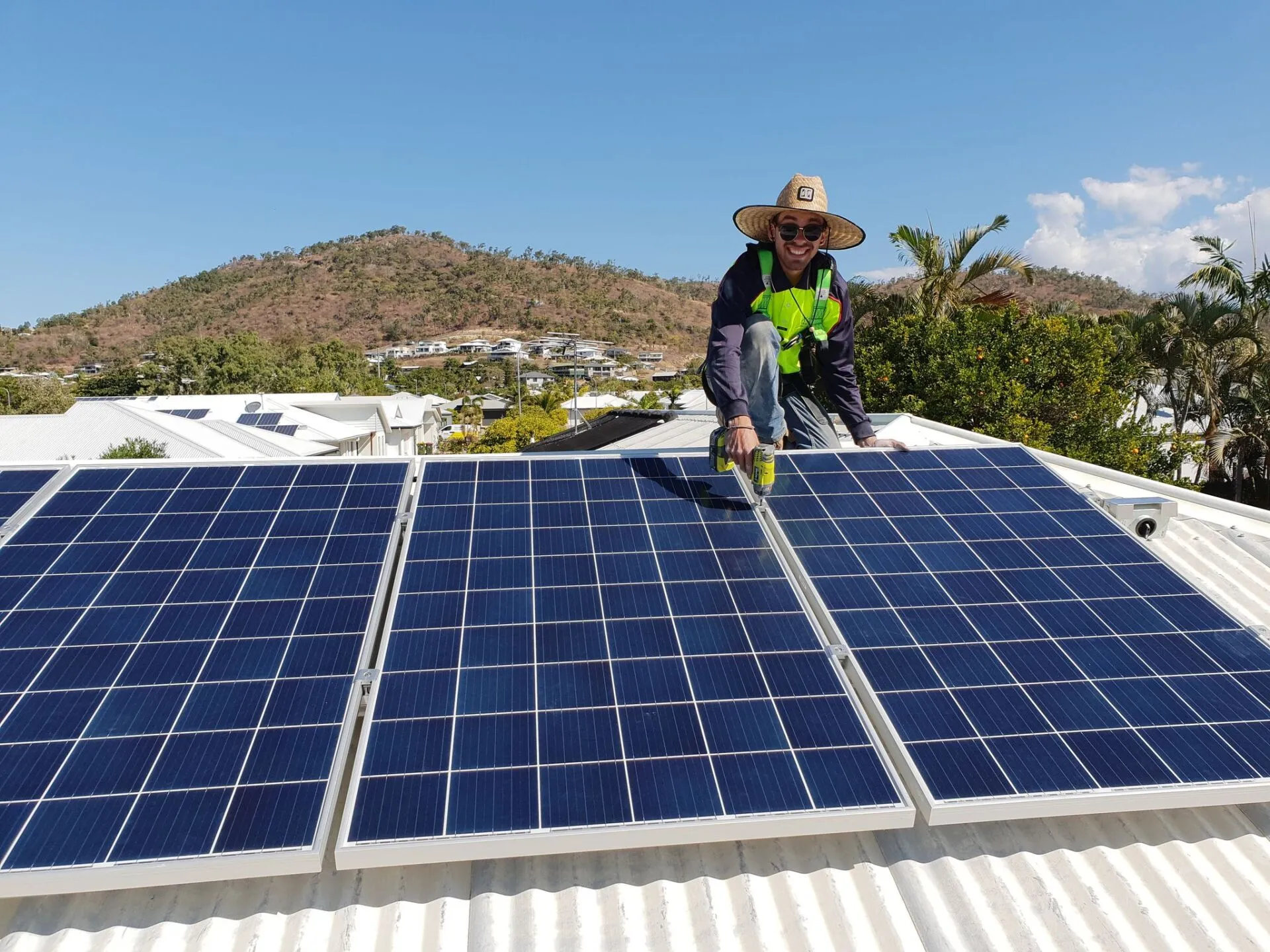 On Point Solar & Electrical technician installing rooftop solar panels on a Townsville home, with the North Queensland hills behind