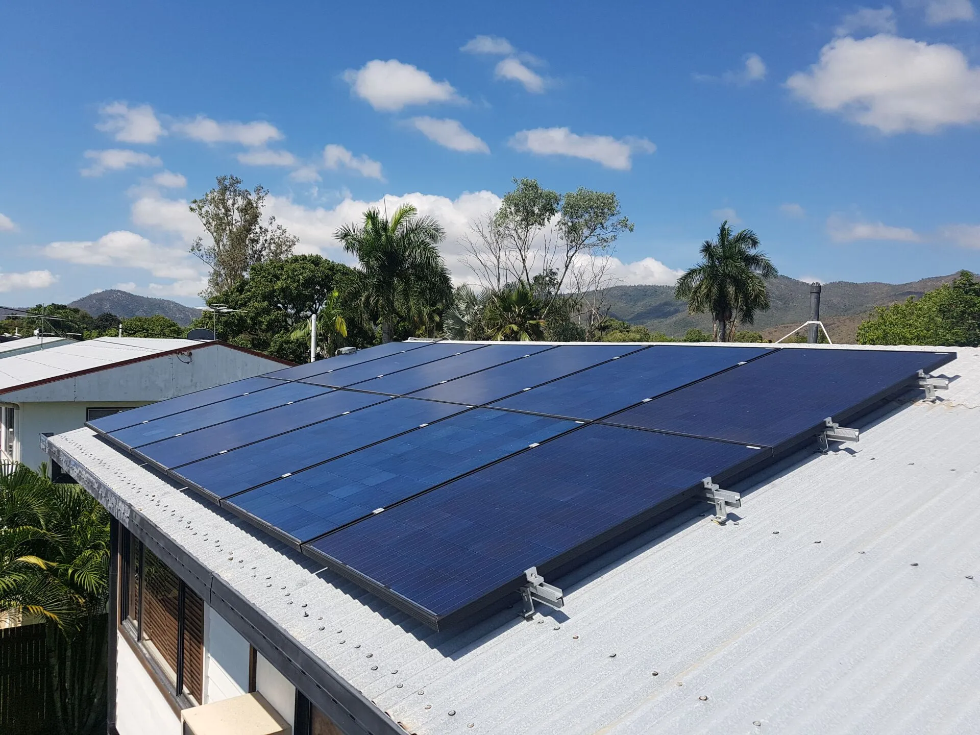 Solar Townsville install by On Point — a rooftop solar panel array on a local home with palm trees and a mountain backdrop