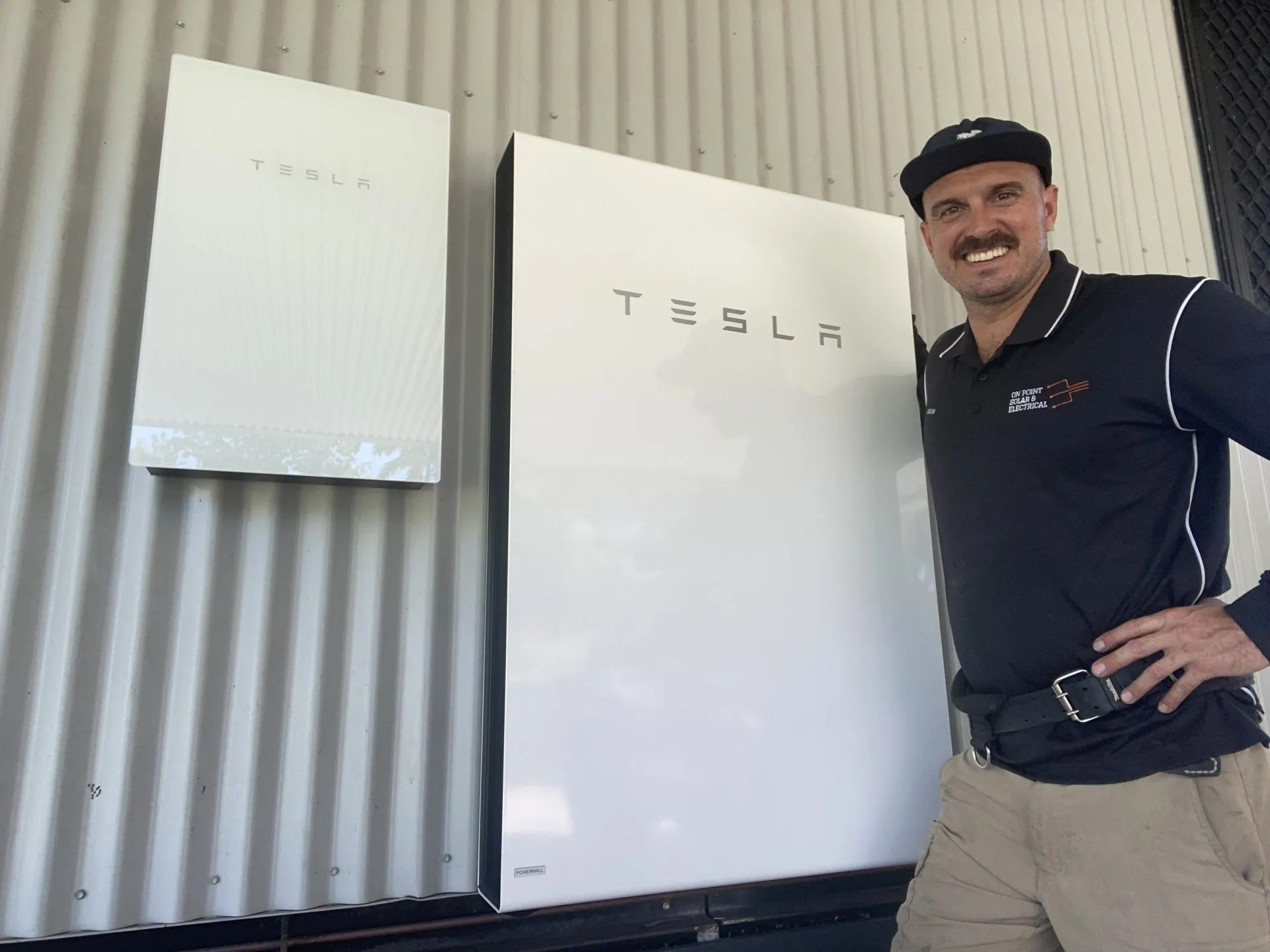 On Point Solar & Electrical owner beside two Tesla Powerwall batteries installed at a Townsville property